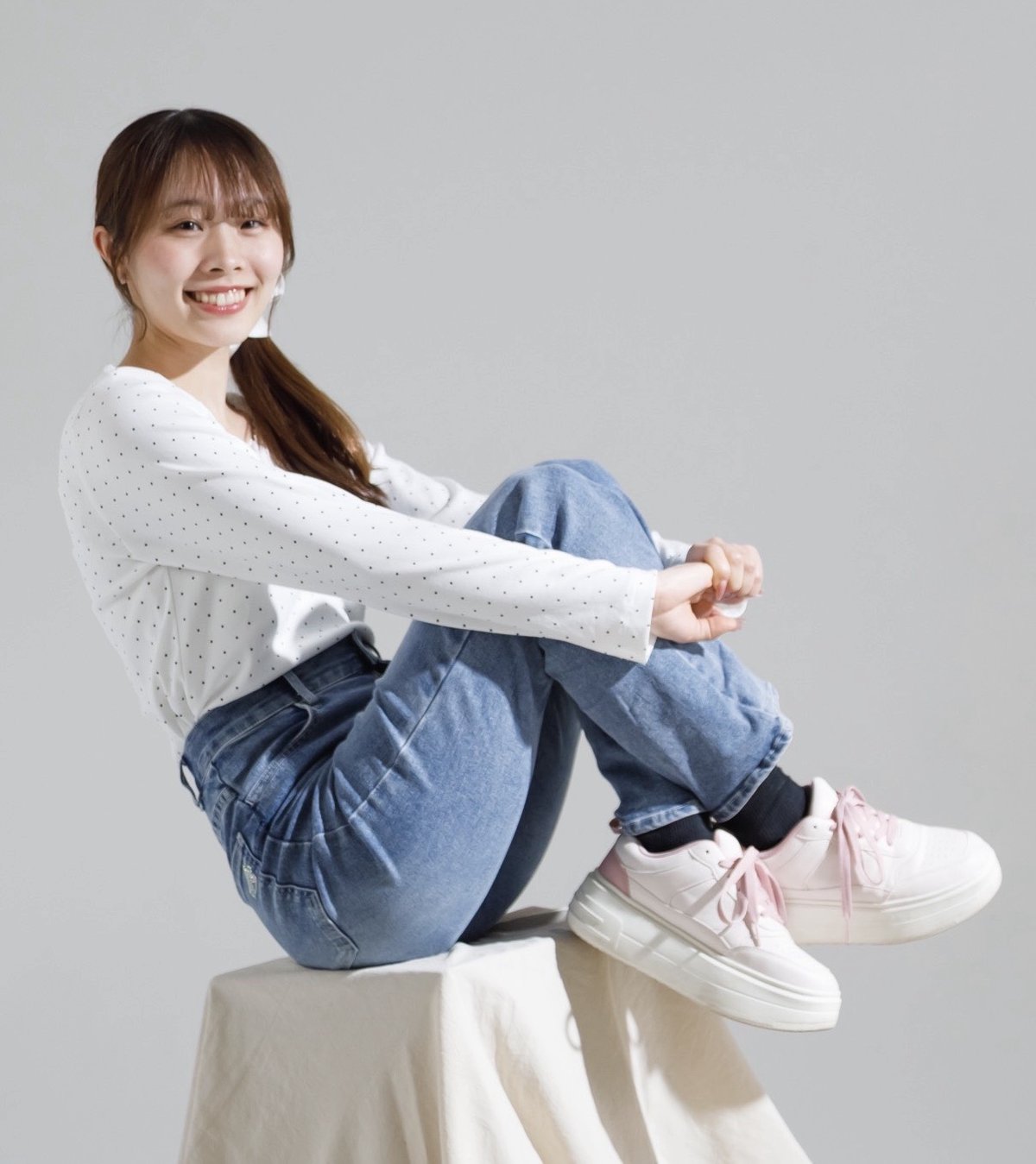 白い台に腰かけ、膝を抱えて笑う叶愛